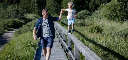 Barn som går balansgång på ett räcke och pappa som håller barnet i handen