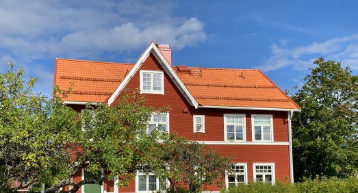 Rött trähus med tegeltak och vita detaljer inbäddat i grönska.