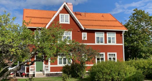 Rött trähus med tegeltak och vita detaljer inbäddat i grönska.
