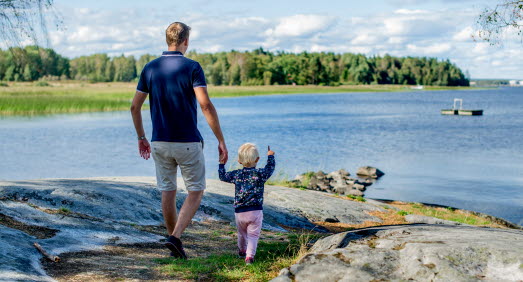 Pappa och barn håller varandra i handen och blickar ut över vattnet. Barnet pekar ut mot vattnet. 