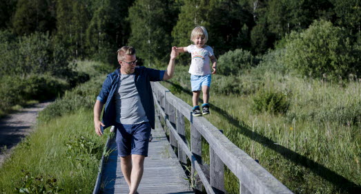 Barn som går balansgång på ett räcke och pappa som håller barnet i handen