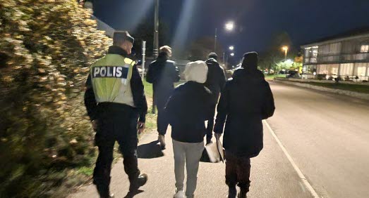 En grupp människor går längs gata på kvällen.