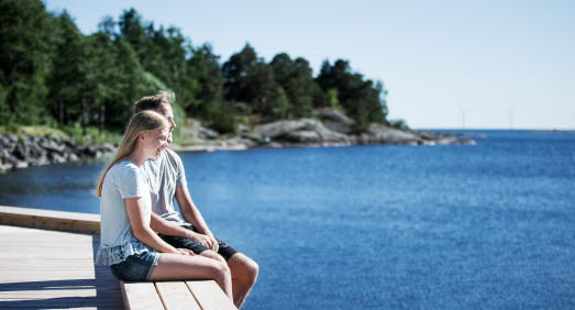 Tjej och kille sitter bredvid varandra på en brygga vid vattnet