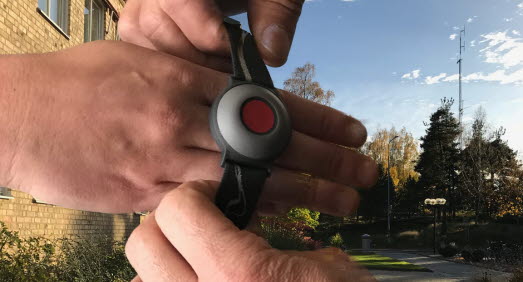 Bild på händer där en person trär på en annan person en larmklocka till ett trygghetslarm