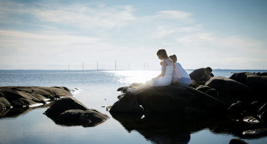Flera personer sitter på klipporna vid det stilla vattnet. 