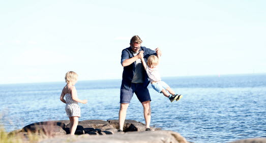 Pappa och två barn leker vid klipporna