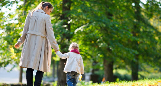 Mamma och dotter går hand i hand i en park full av höstlöv