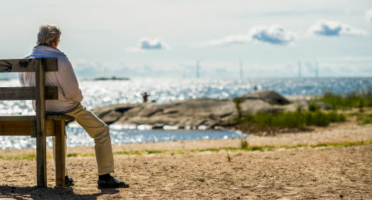 Människa sitter på en bänk på stranden och blickar ut över vattnet och klipporna