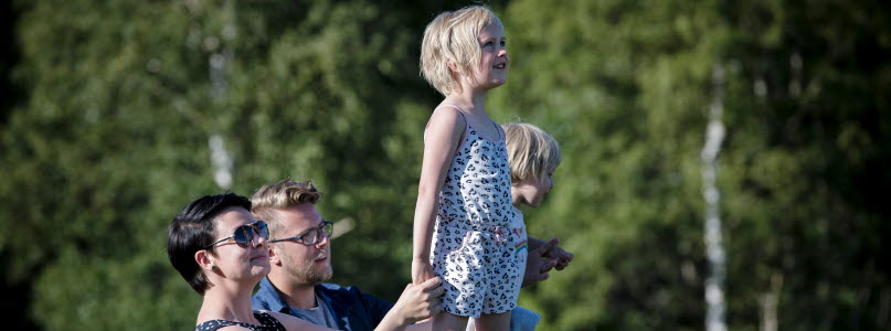 Mamma och pappa som håller i sina barn som står på ett räcke och blickar ut. 