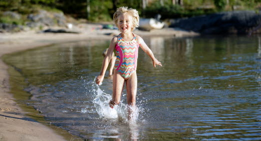 Barn springer i vattnet, vid strandkanten. 