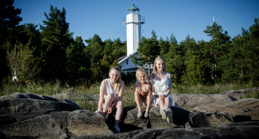 Tre tjejer sitter bredvid varandra på klipporna. I bakgrunden ser man Skage Fyr. 