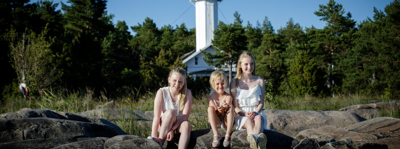 Tre tjejer sitter bredvid varandra på klipporna. I bakgrunden ser man Skage Fyr. 